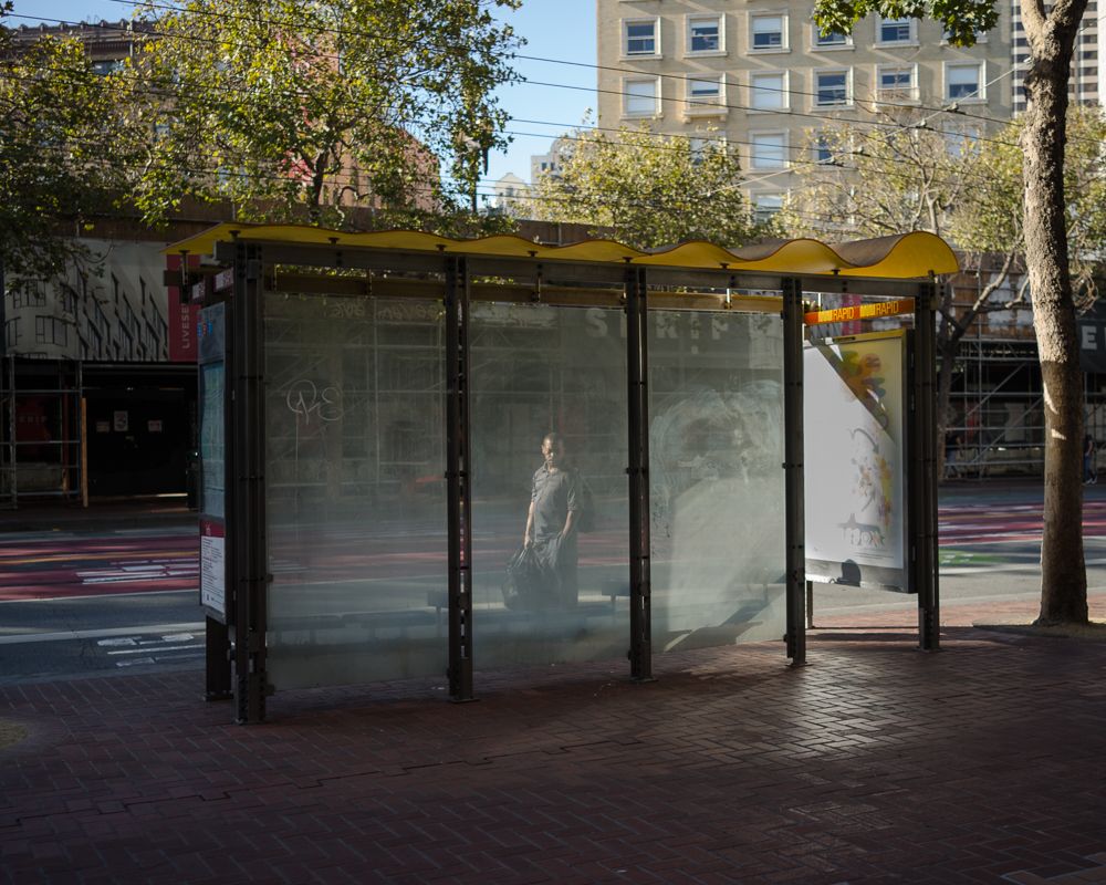 Empty glass bus shelter on urban street with mysterious reflection.