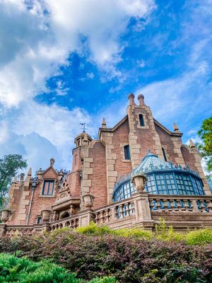 The Haunted Mansion attraction at Disney World showcases Gothic Revival architecture with pink stone and blue glass dome details.