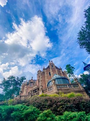 Gothic-style castle architecture of Disney's Haunted Mansion rises against a bright blue sky with puffy white clouds.