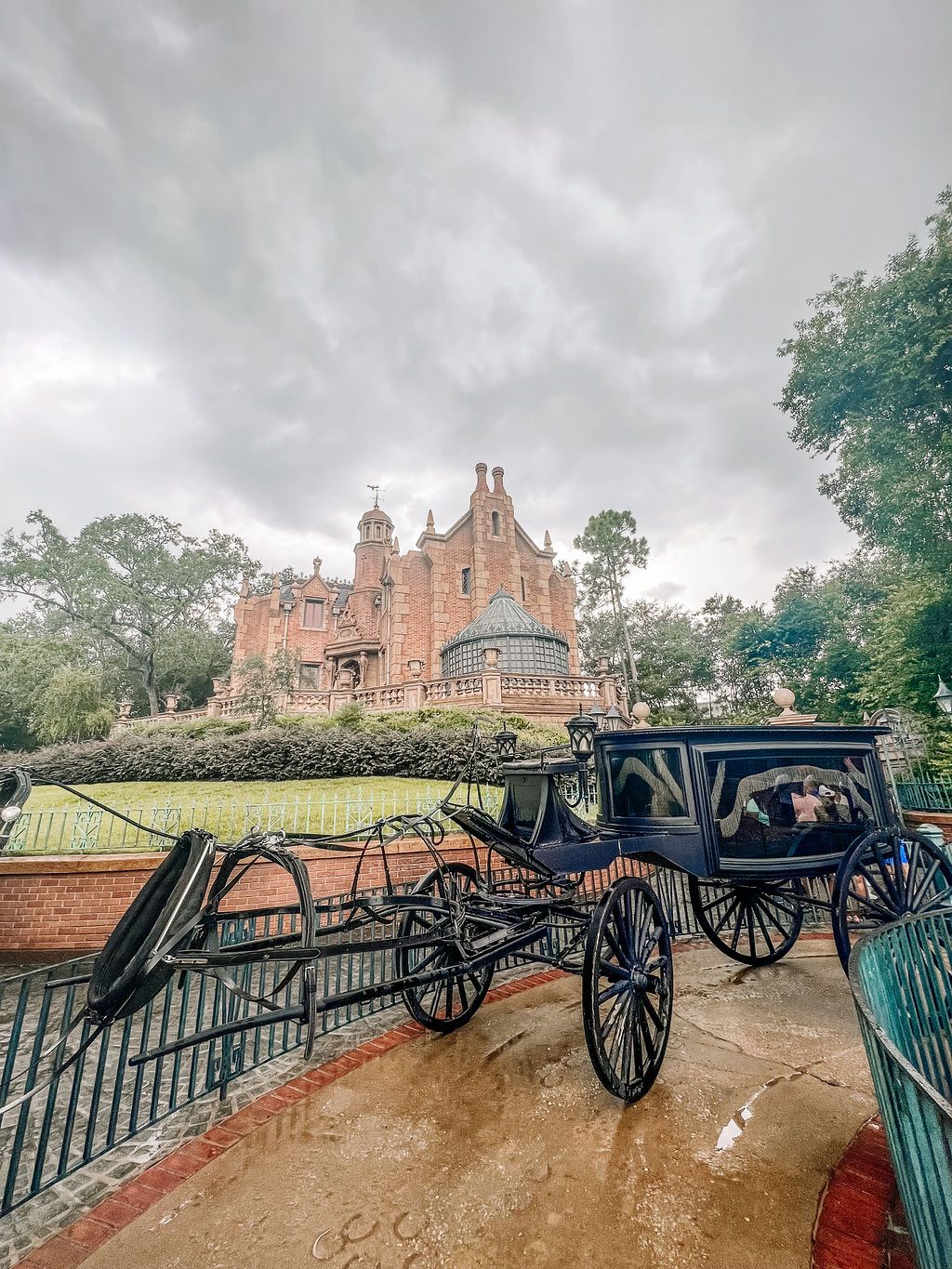 A horse-drawn carriage stands in front of the Gothic-style Haunted Mansion attraction at Disney's Magic Kingdom on a cloudy day.