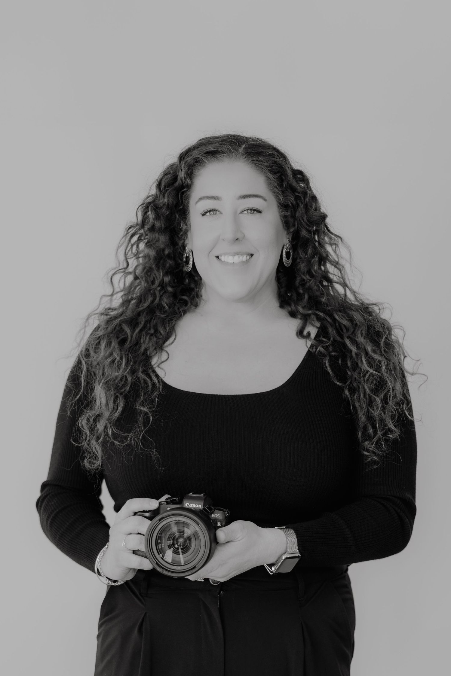 Professional photographer with curly hair holding camera in black and white portrait.