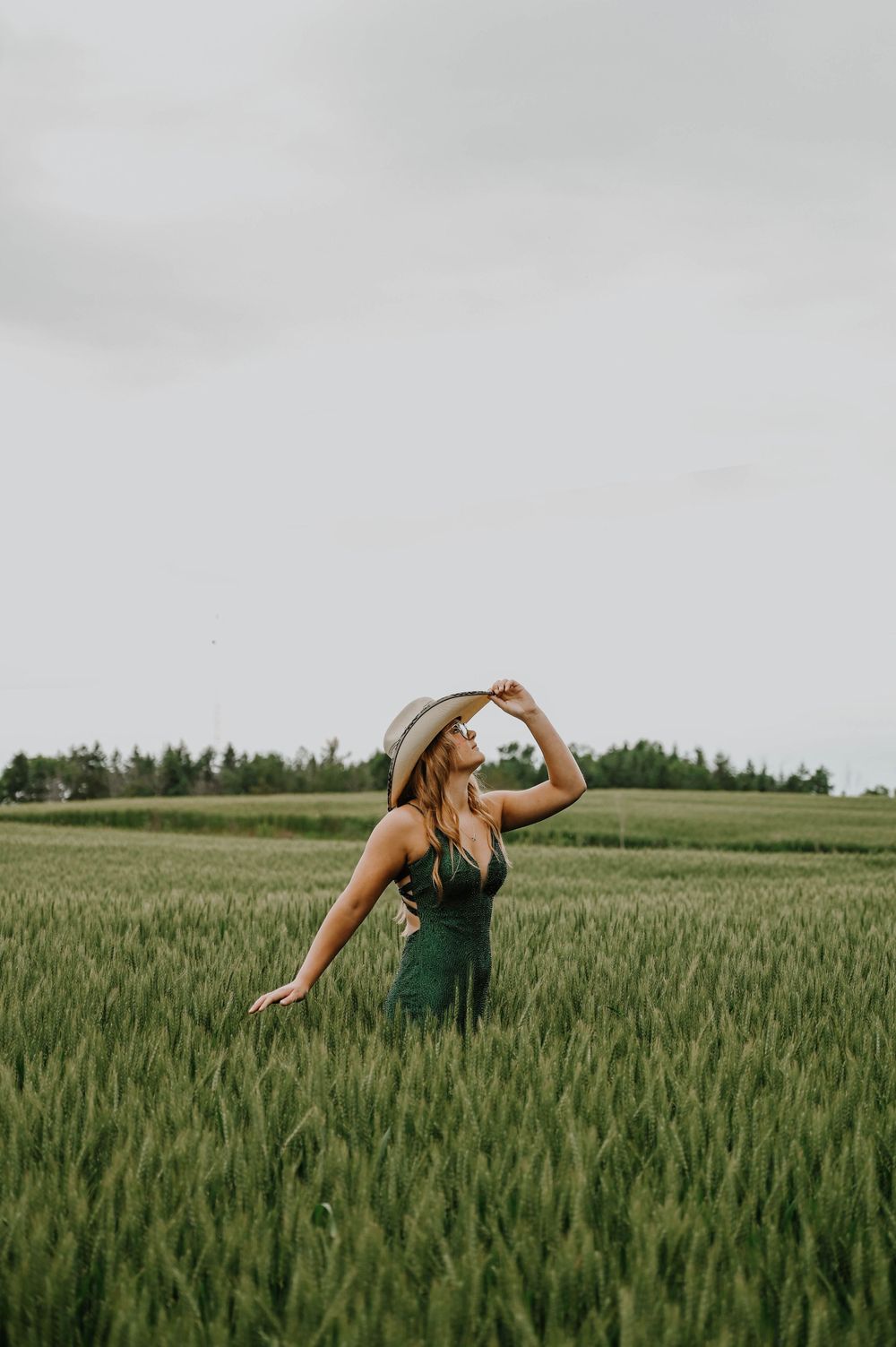 A figure in a green dress dances through a lush wheat field on an overcast summer day.