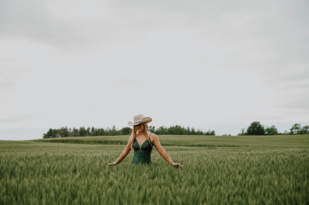 Person in green dress stands in middle of lush wheat field on cloudy summer day.