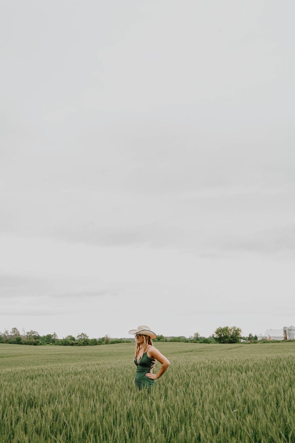 Person in a green top stands contemplatively in a vast wheat field under an overcast sky.