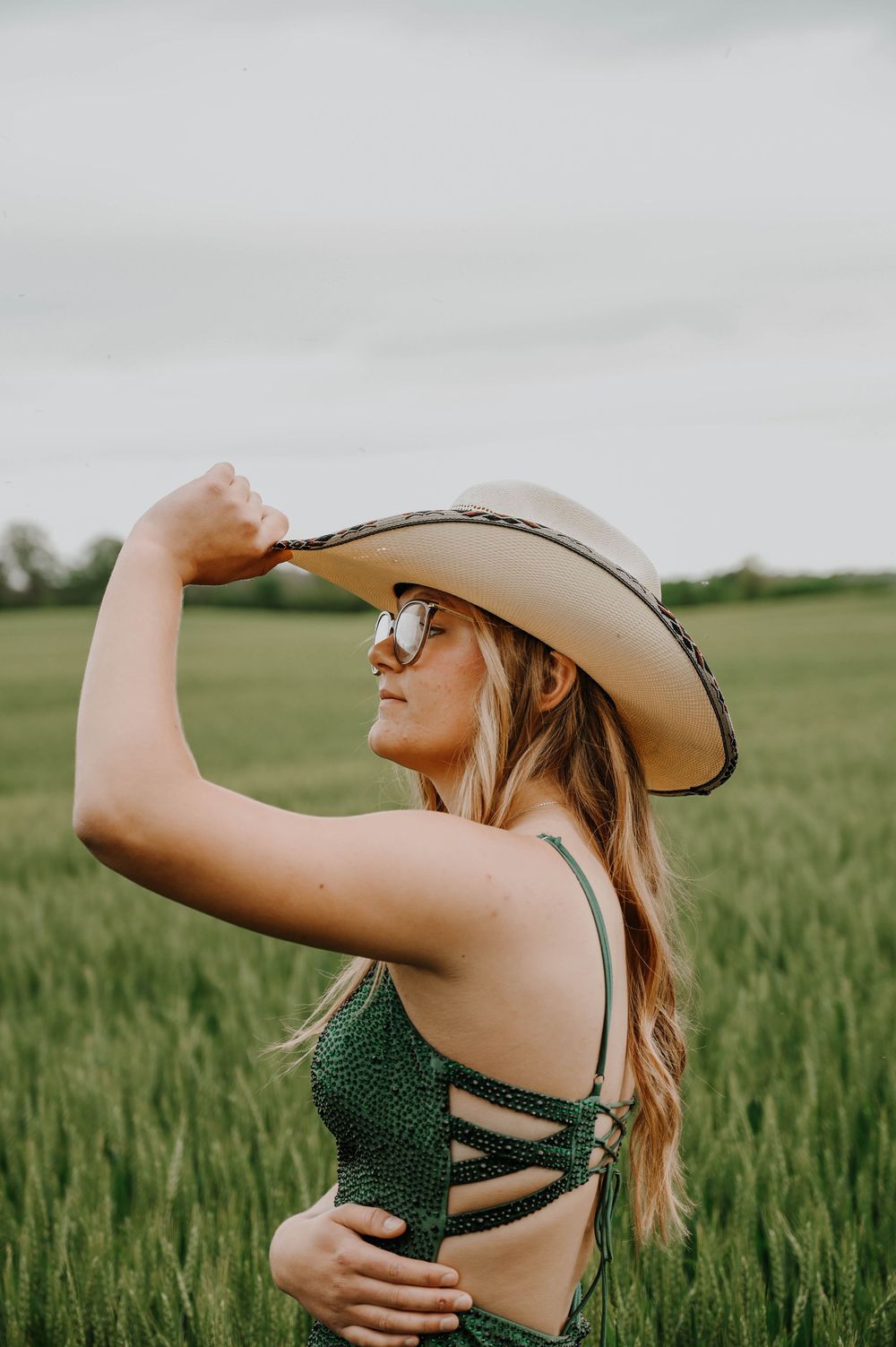 Woman in sparkling green swimsuit and cowboy hat poses in a wheat field during golden hour.