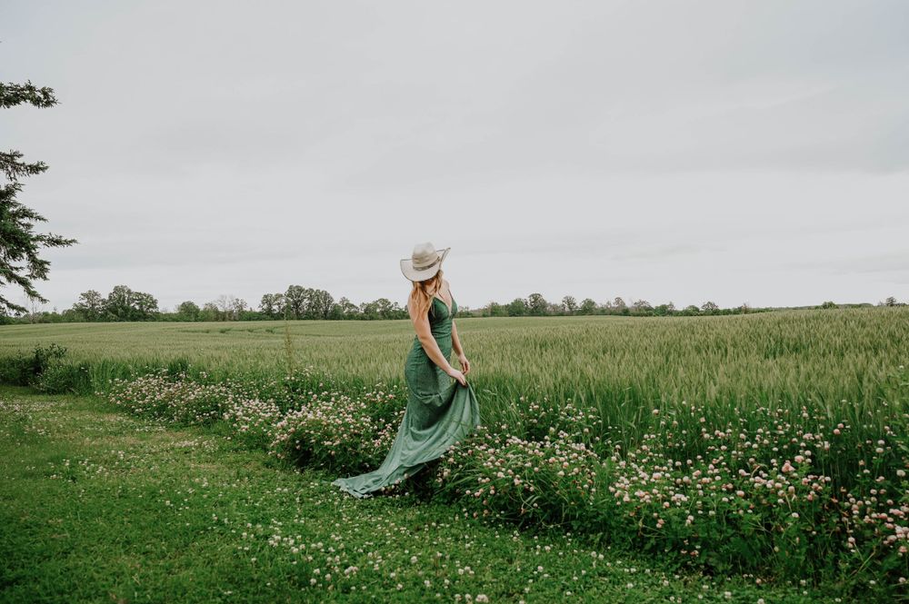 Woman in flowing green dress walks through a wildflower meadow on an overcast day.