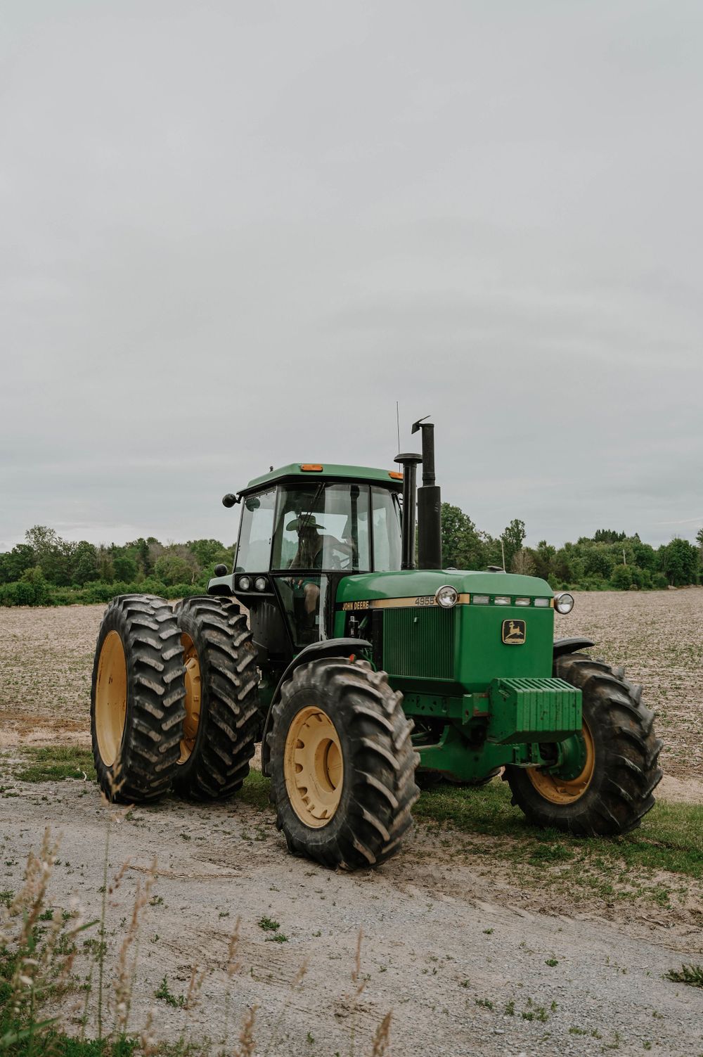 A classic green John Deere 4440 tractor with large dual rear wheels parked on dirt ground under an overcast sky.