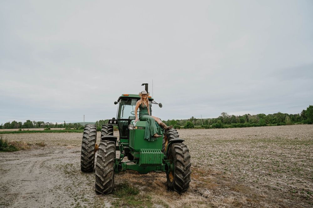 A green John Deere tractor stands in a muddy field under an overcast sky.