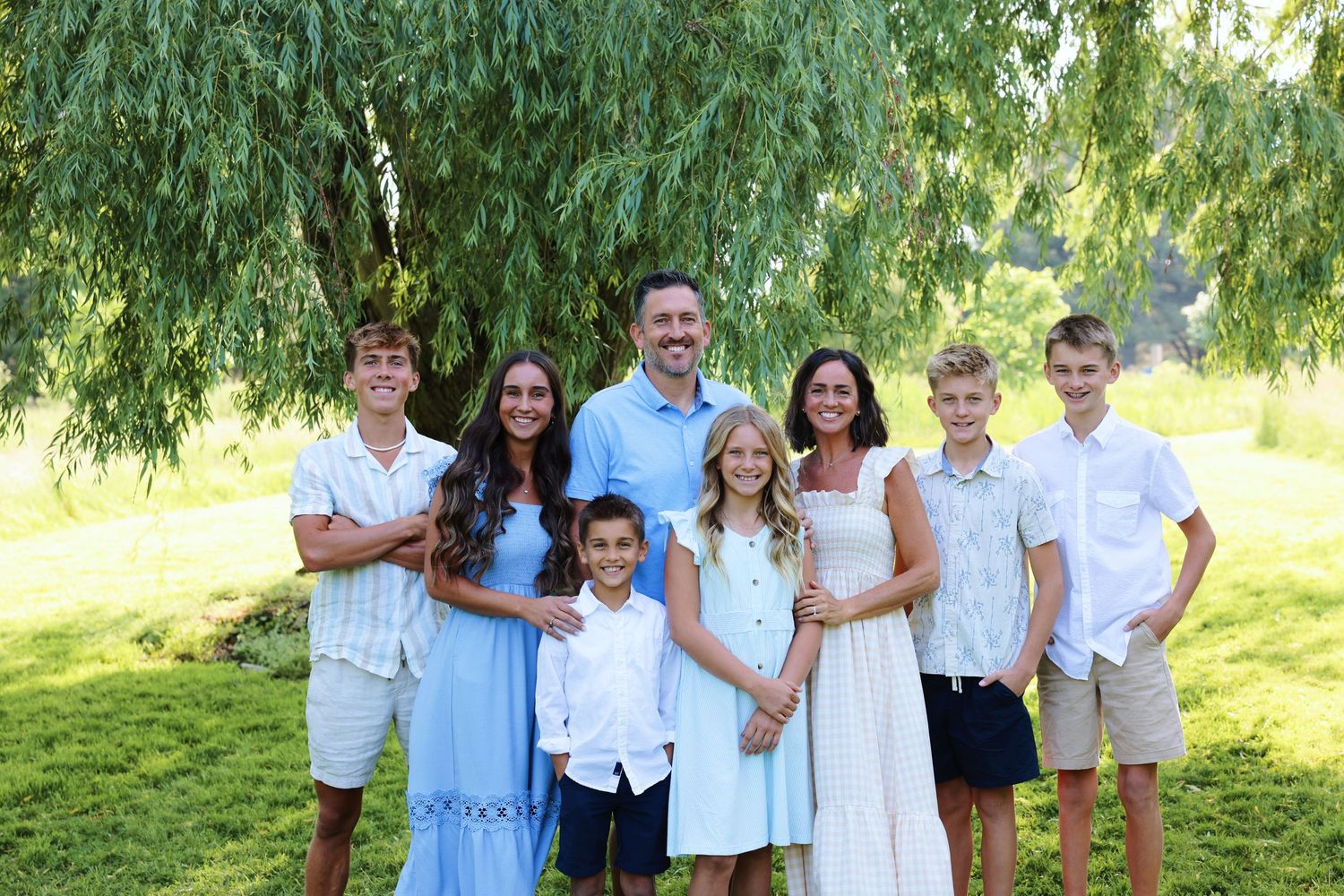 Group photo of six people wearing casual summer attire standing together in wooded setting.