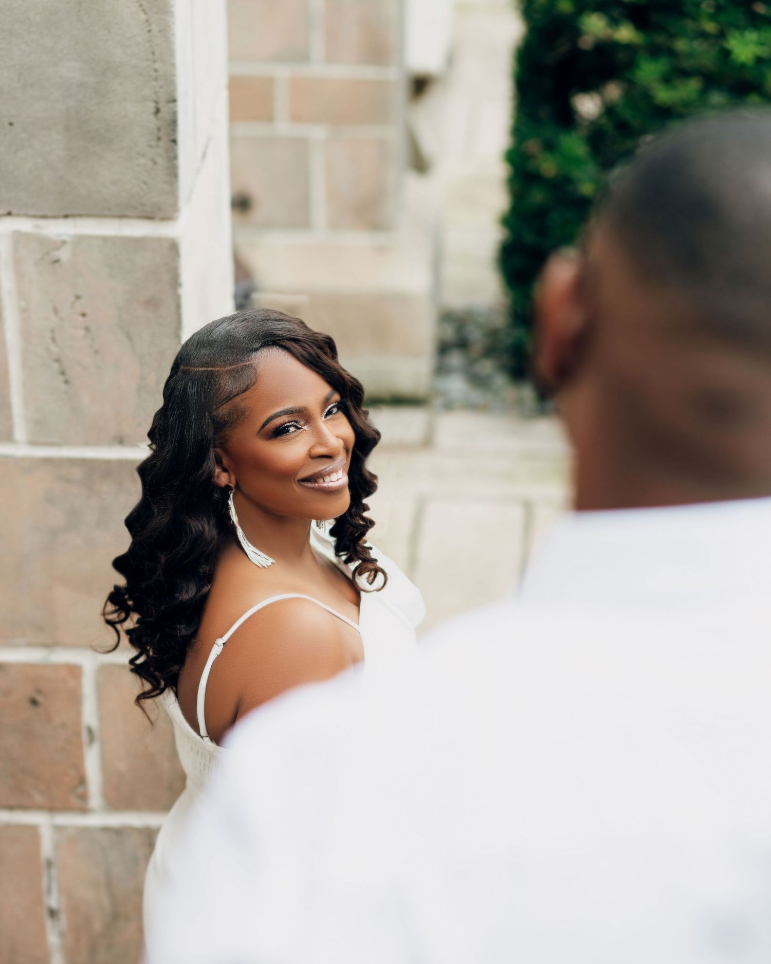 A beautiful bride in a white wedding dress smiles over her shoulder during a romantic outdoor photoshoot.