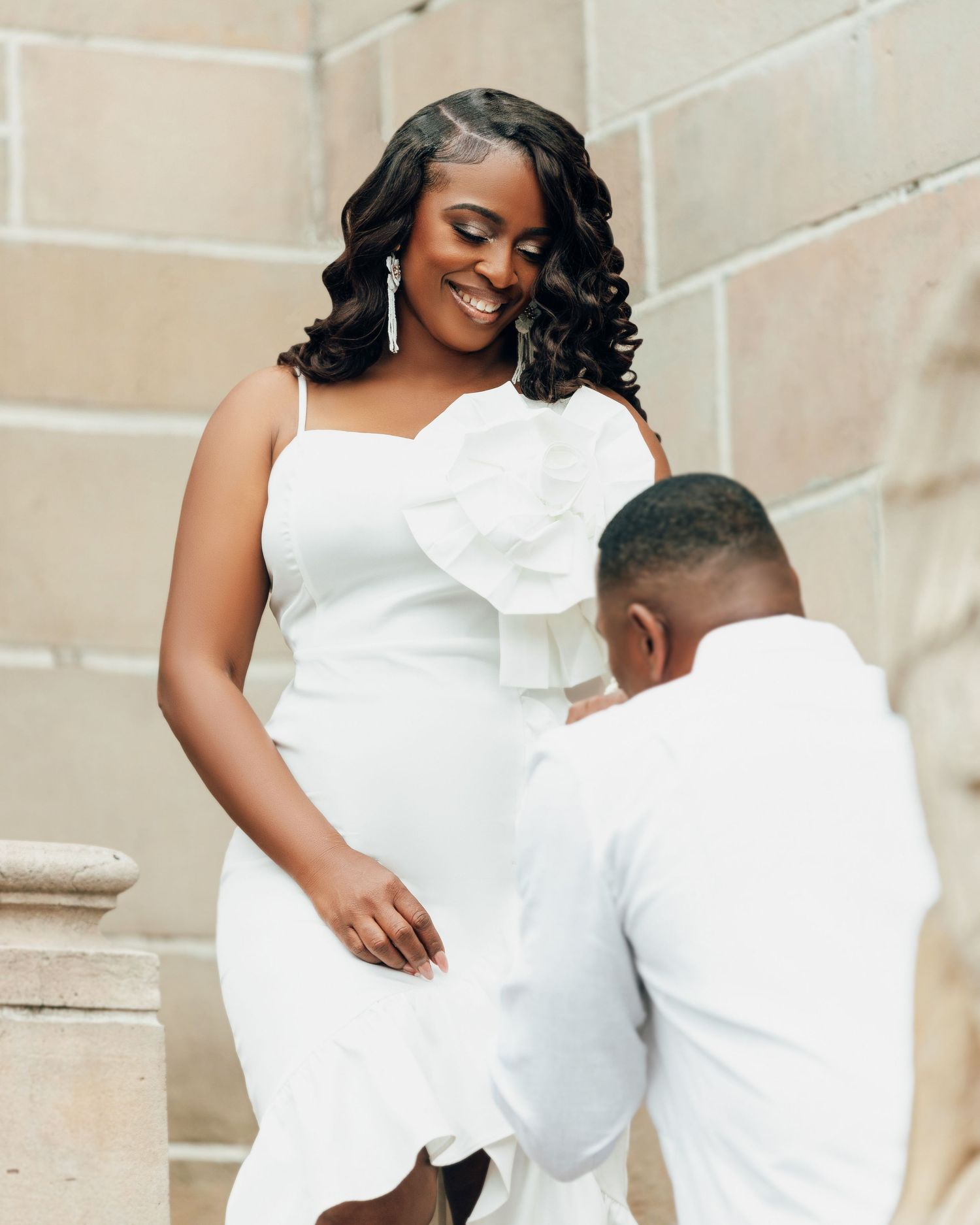 A couple dressed in white sharing a romantic moment together on stone steps against a beige wall.