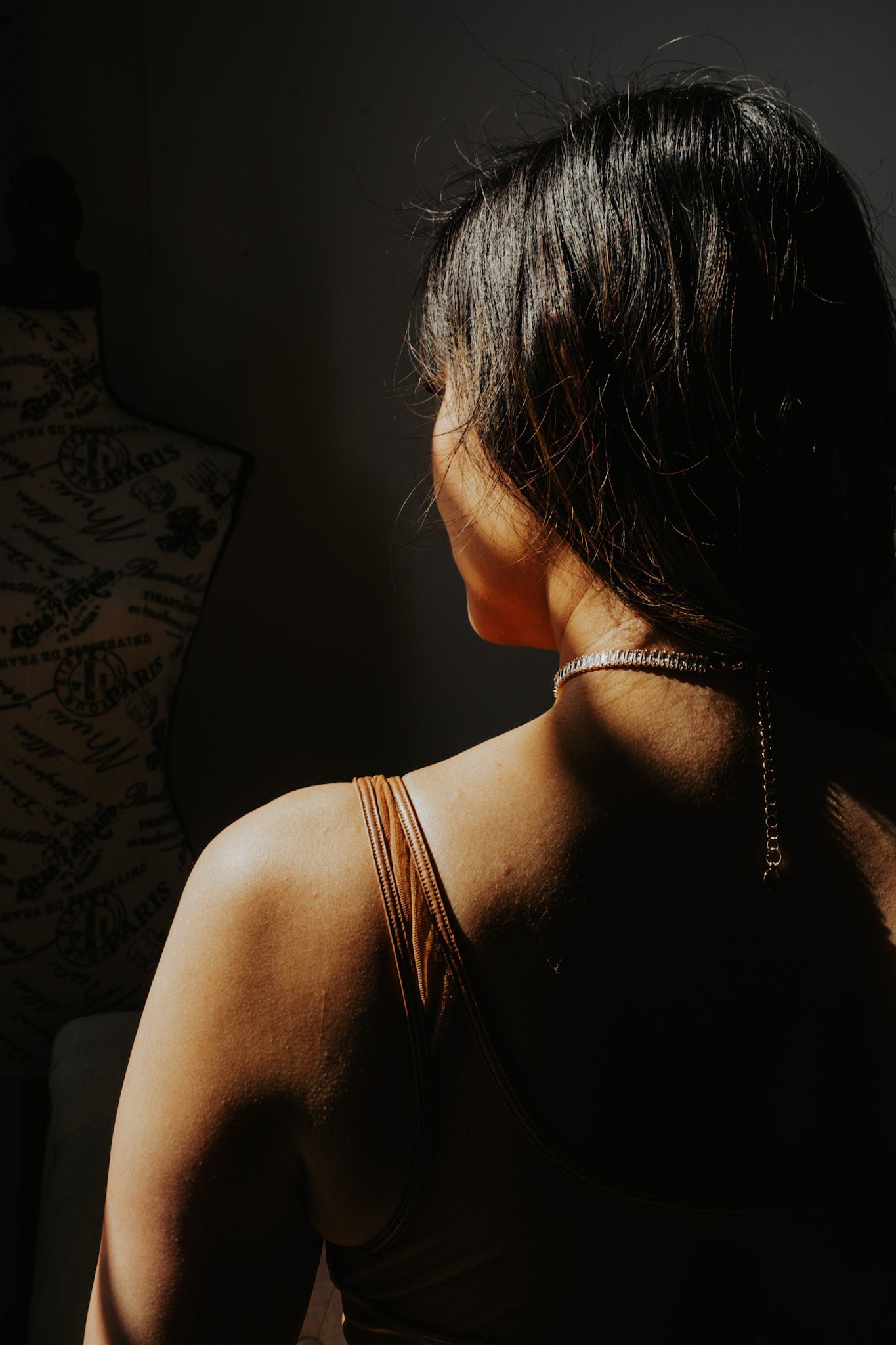 Artistic portrait showing shoulder and neck with delicate chain necklace in dramatic lighting.