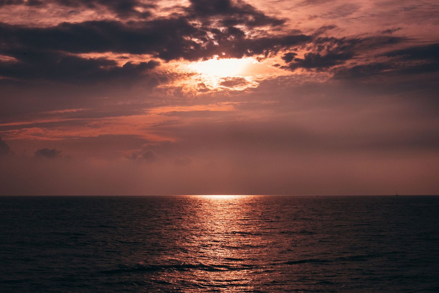 Dramatic orange sunset over ocean waves with sun reflecting on dark water beneath cloudy sky.