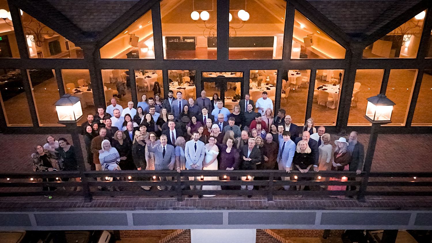 Overhead view of guests gathered outside a timber-framed lodge building in the evening with glowing lights.