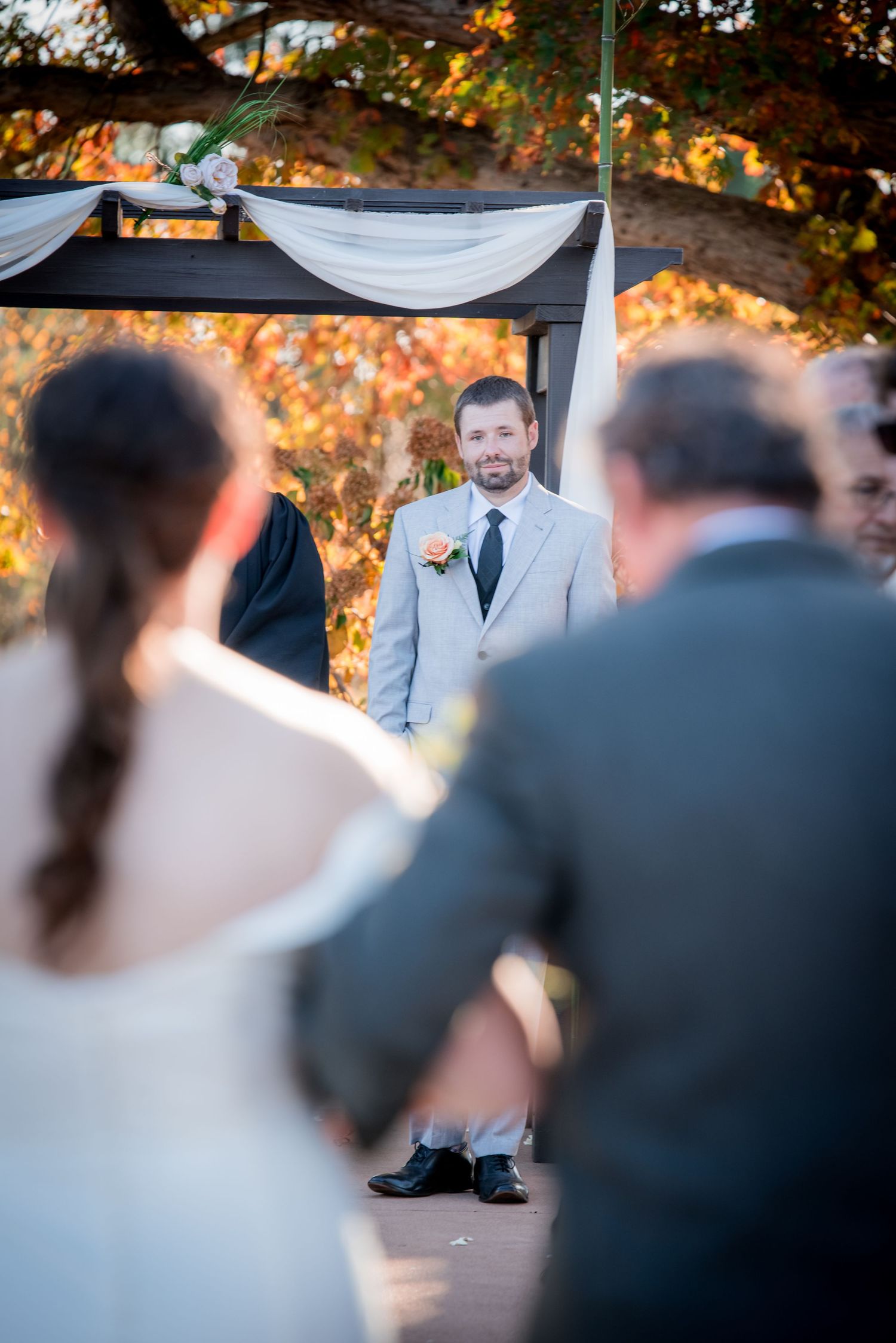 An outdoor wedding ceremony under autumn trees with white fabric draping.