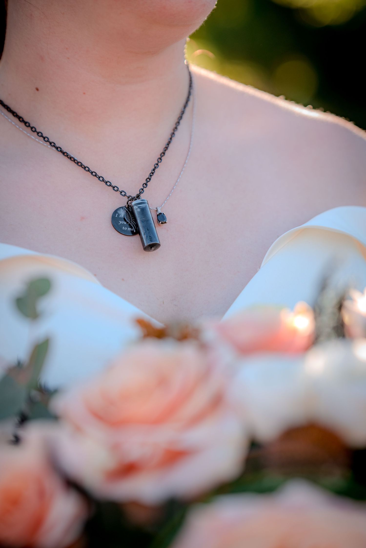 A delicate dark metal necklace with a toggle clasp pendant photographed against blurred pink roses in the background.