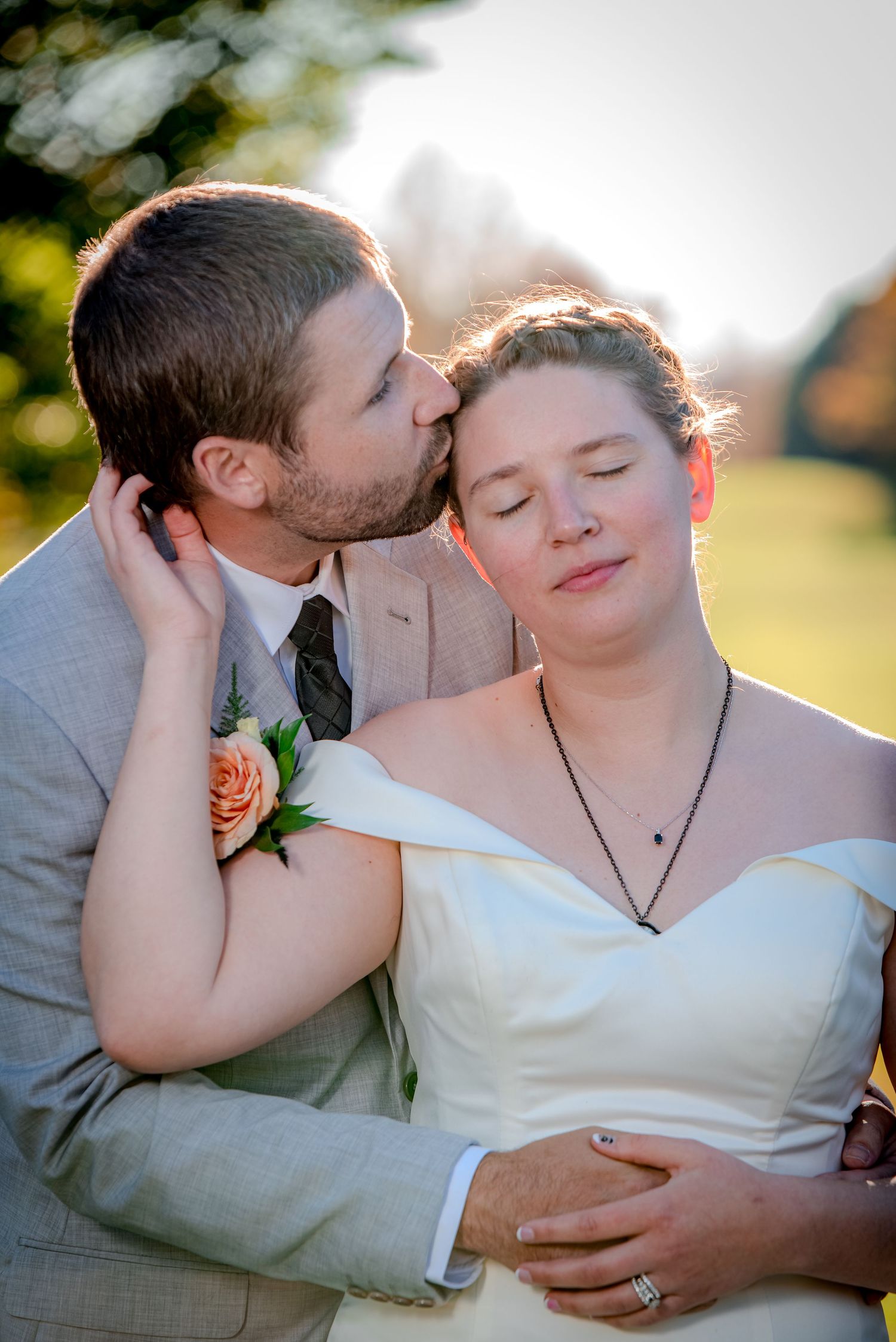 A romantic moment between newlyweds captured in golden sunlight with peach rose boutonniere details.