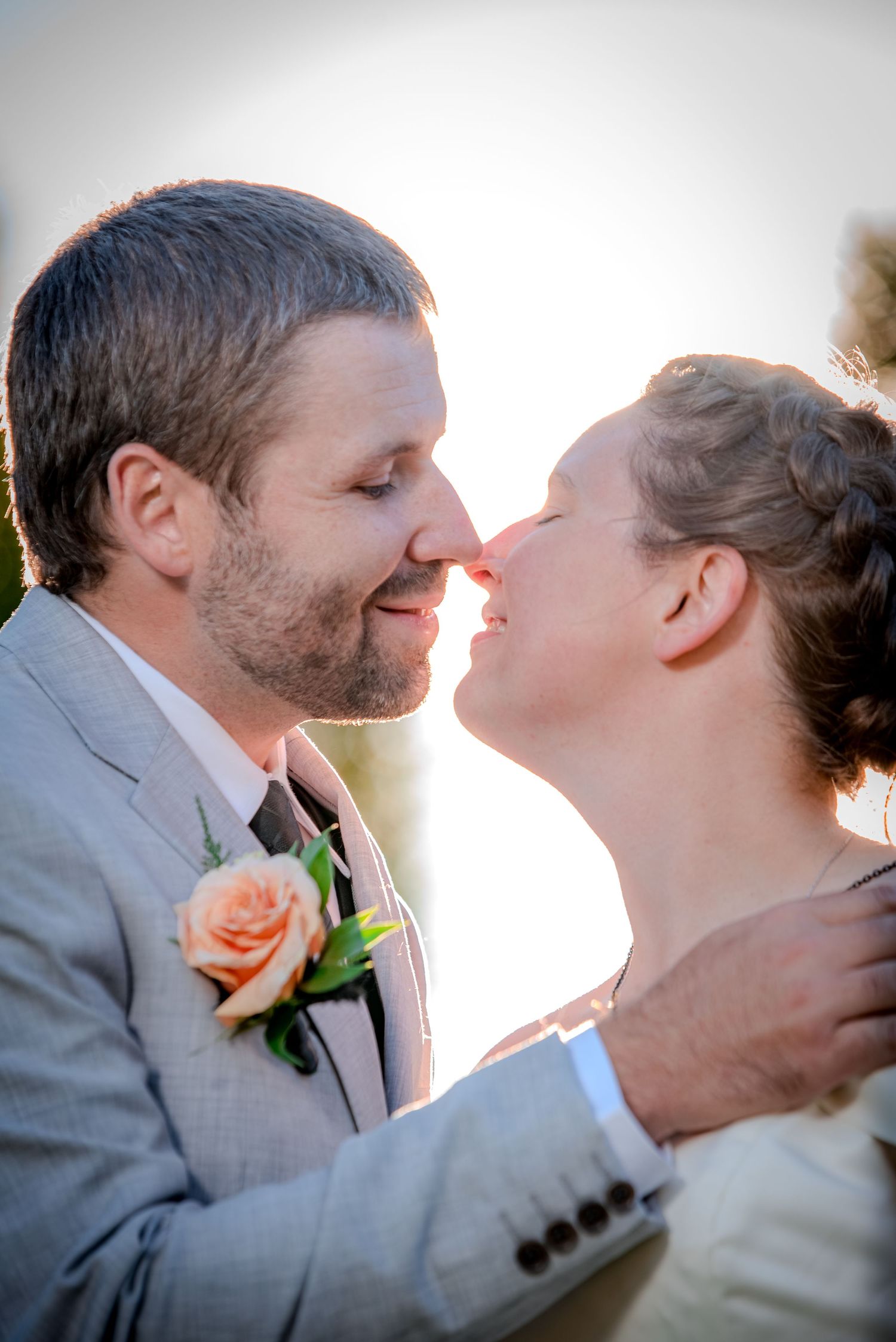 Romantic sunset moment between newlyweds with a peach rose boutonniere and soft lighting.