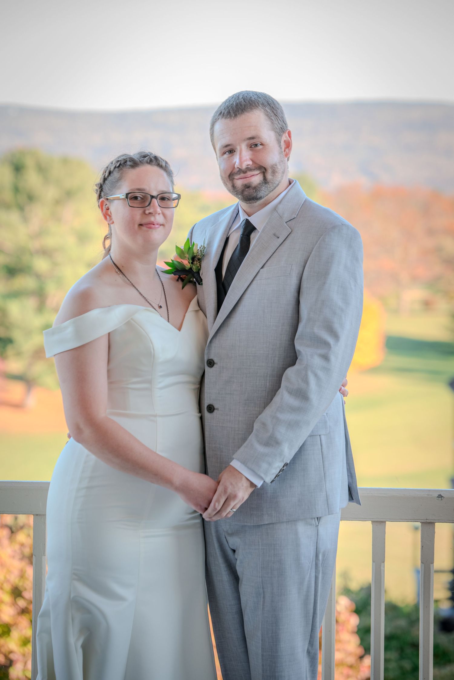A couple poses together on a deck with autumn foliage visible in the mountain background.