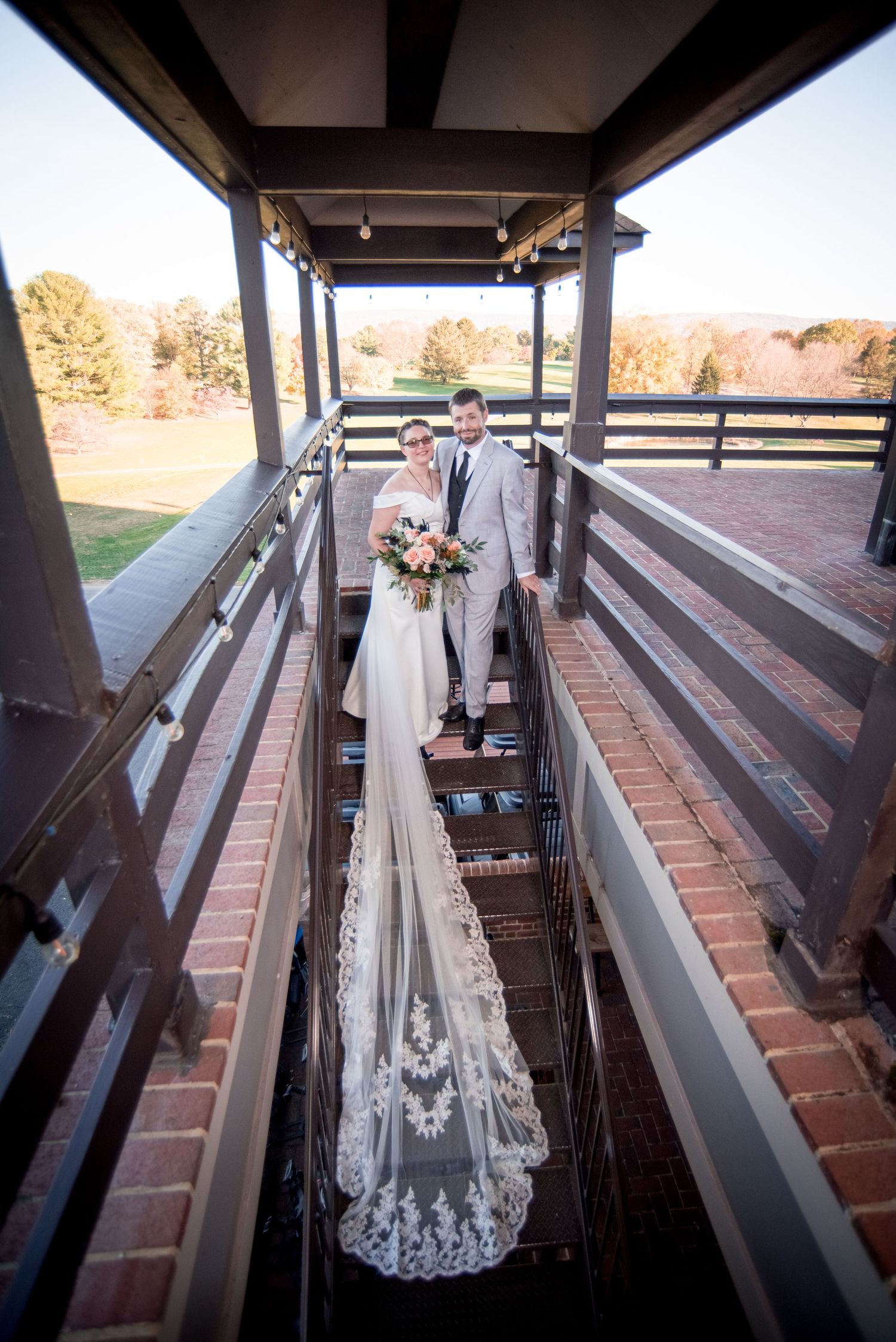 A dramatic overhead view of newlyweds on a covered walkway with a flowing lace veil trailing behind.