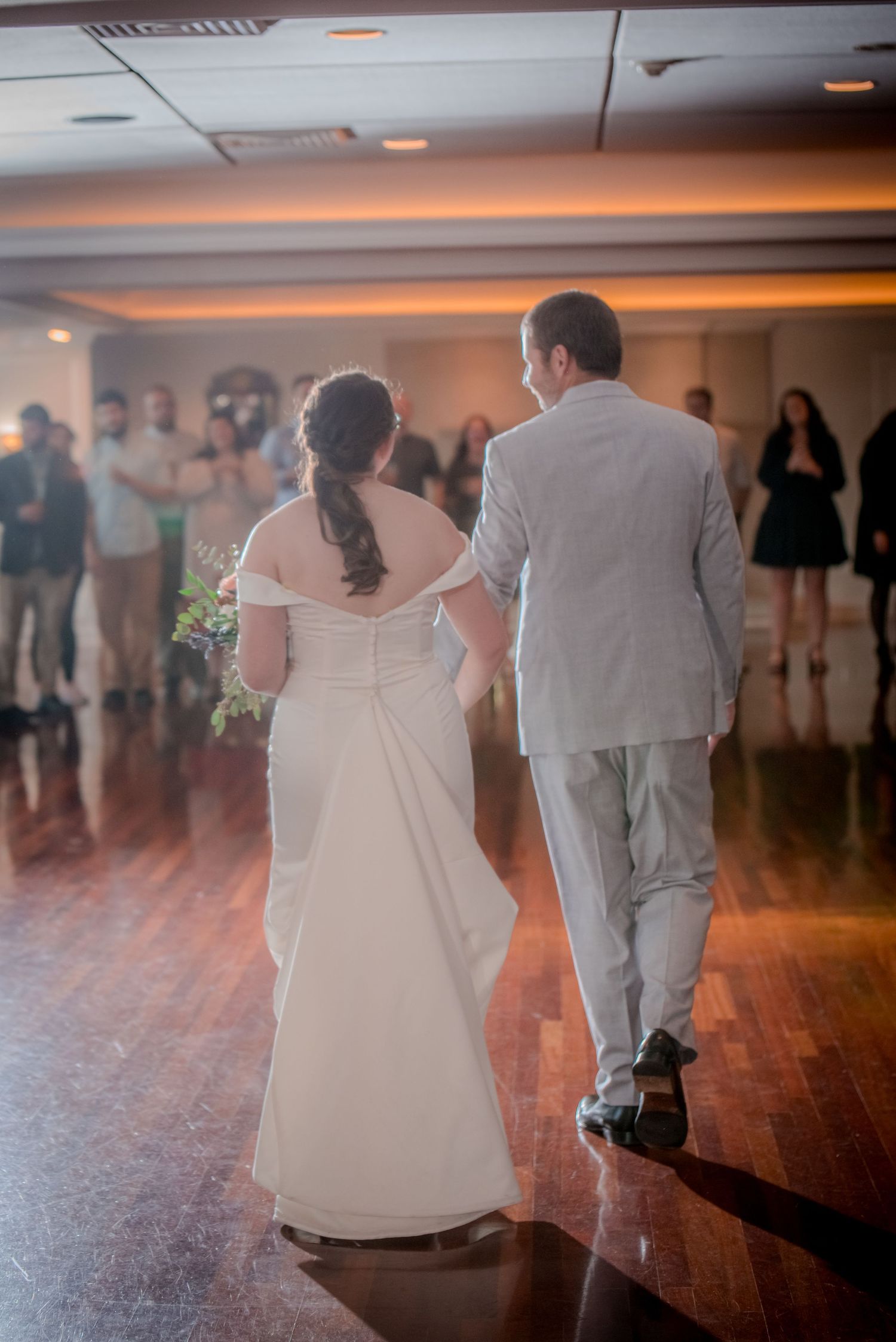 A couple shares their first dance on a polished wooden dance floor at their wedding reception indoors.