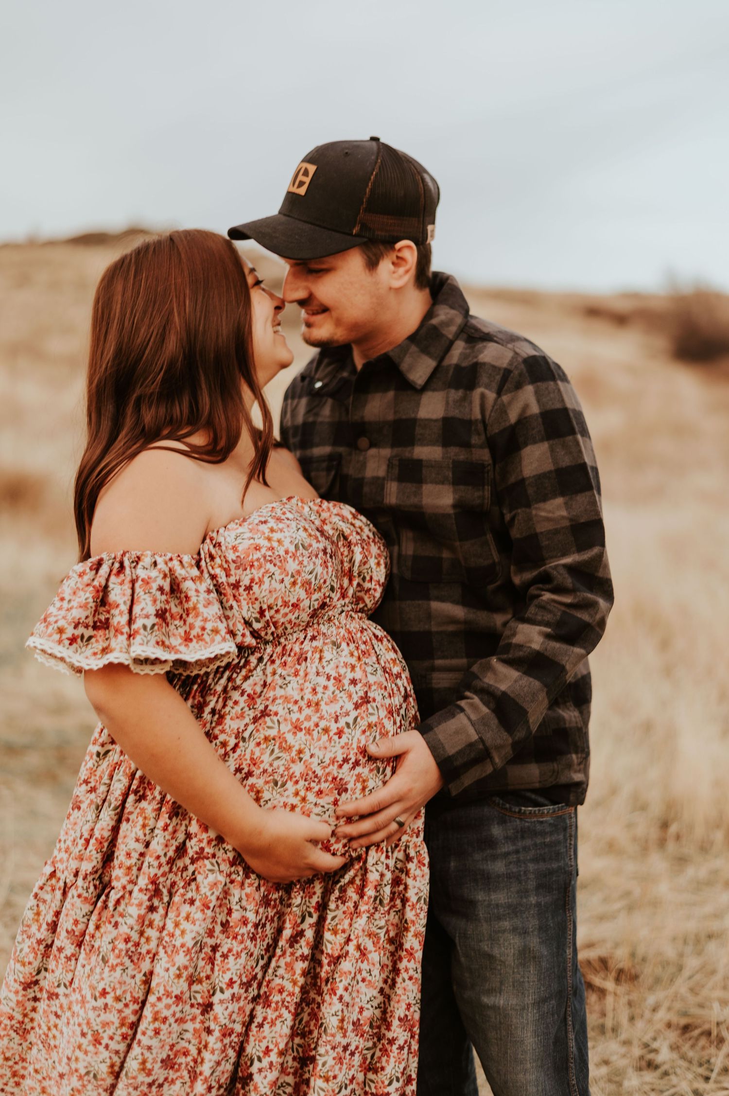 A tender maternity portrait of a couple in casual wear standing in a golden field.