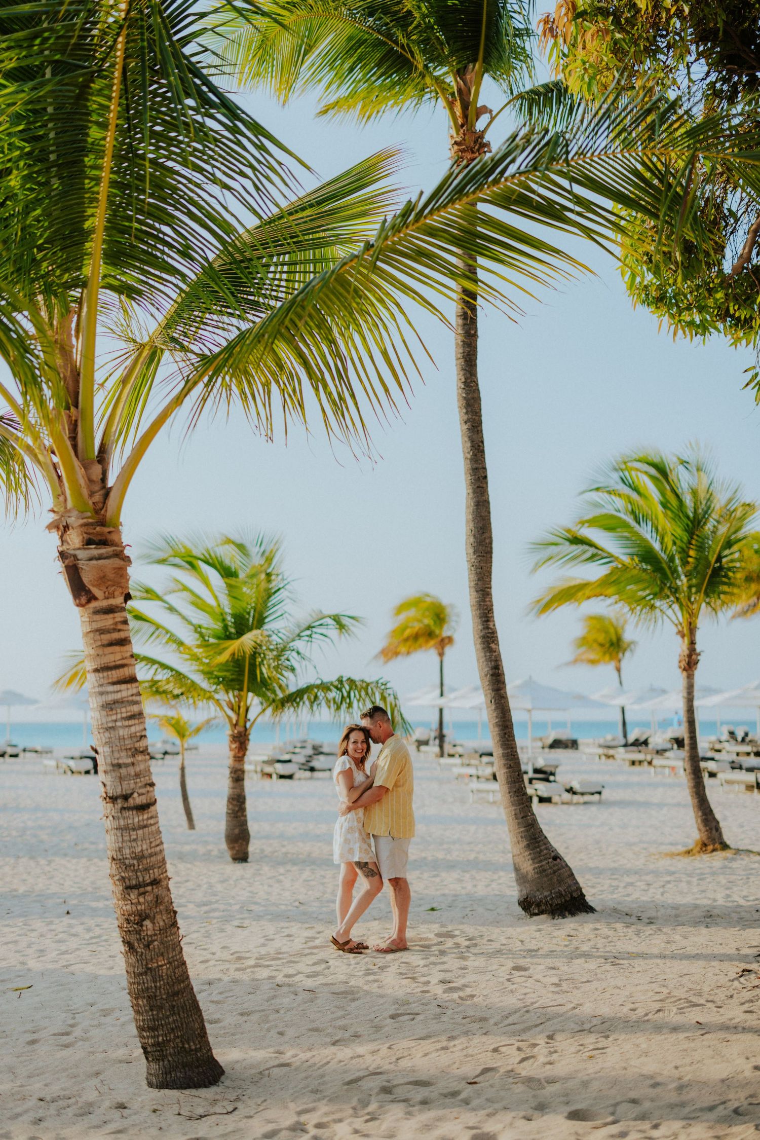 A selfie with a beachy backdrop shows two people in casual attire enjoying a sunny day by the ocean.