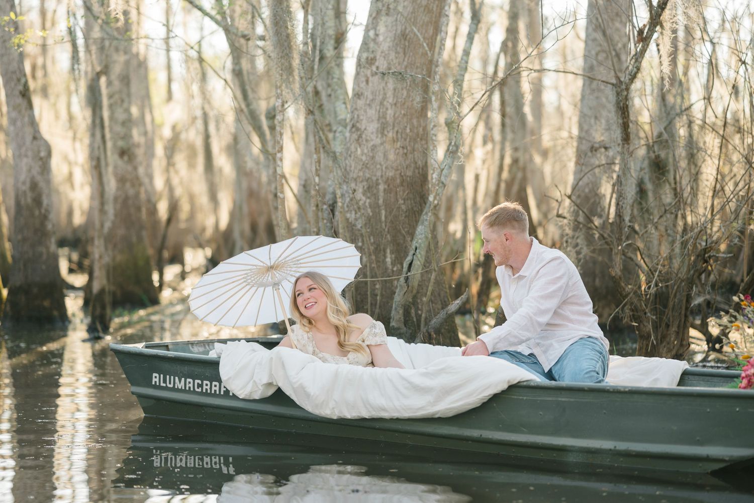 A couple embraces in a playful pose on a grassy field with oak trees in the golden afternoon light.