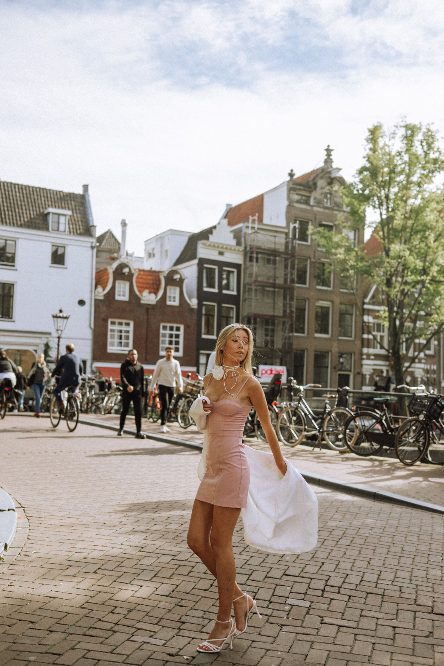 Woman in pink dress walking across Amsterdam square with historic buildings and bicycles.