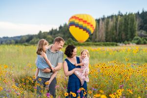Family laughing together with hot air balloon in the background in a flower field.
