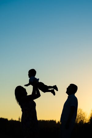 Silhouette photo at sunset of a family throwing child into the air.