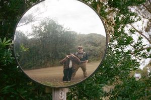 A convex traffic mirror on a pole reflects a dirt path surrounded by green foliage.