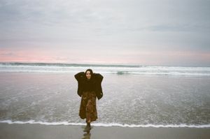 A person walks along a misty beach at sunset while waves crash on the shore.