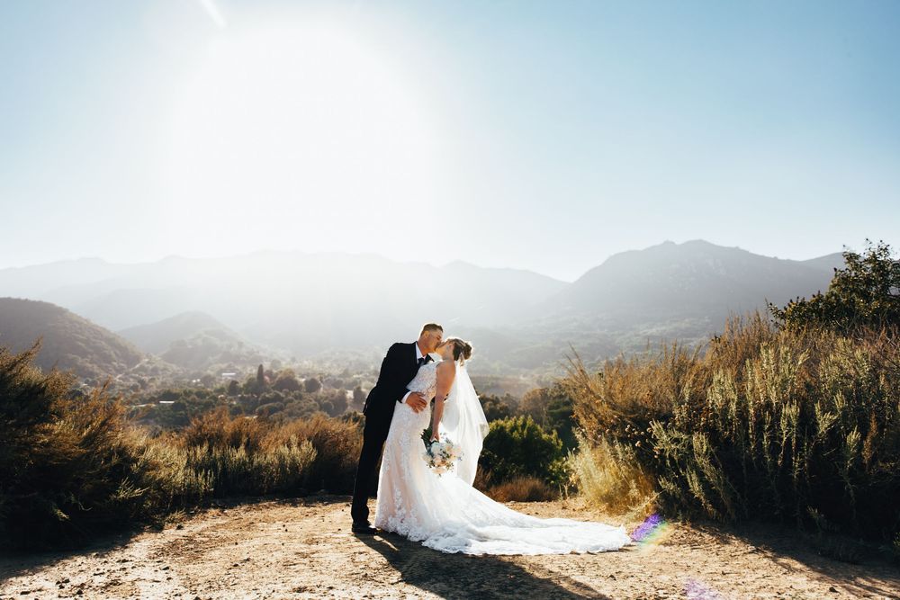 A couple shares a romantic moment on a hilltop overlooking mountains during a sunset wedding photoshoot.