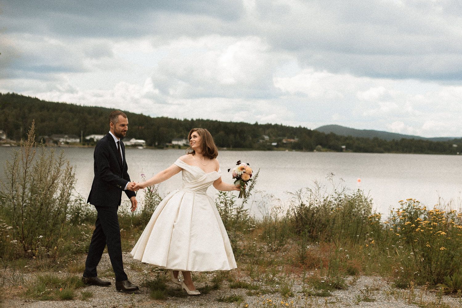 Ett brudpar som går. Kvinnan går före och mannen efter. Hon håller i en brudbukett.