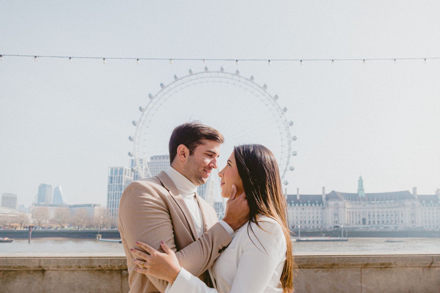 Capture unforgettable moments with a London photoshoot—A loving couple embraces on a bridge with the London Eye and city skyline behind them