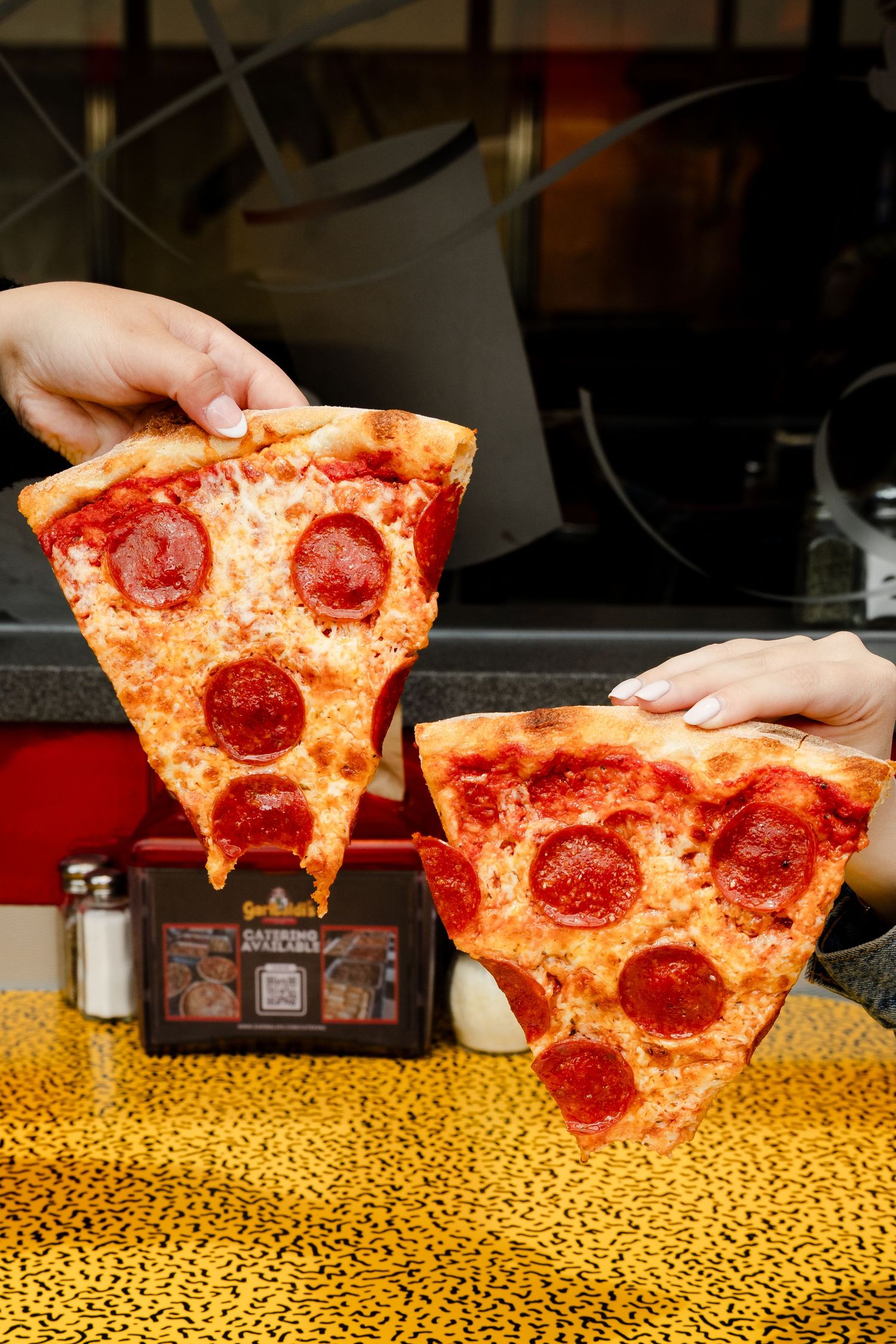 Fresh pepperoni pizza slices being served on a retro patterned yellow counter.