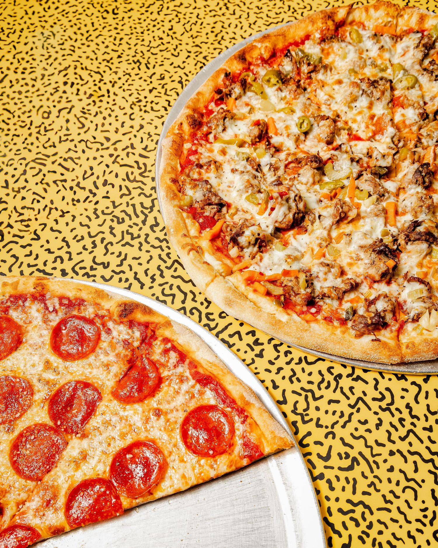 Assorted pizzas with pepperoni and meat toppings on yellow patterned background.