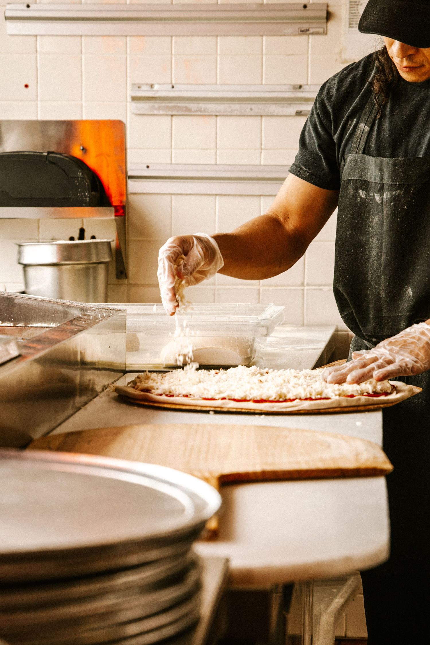 Chef preparing pizza dough on large round metal pans in commercial kitchen.