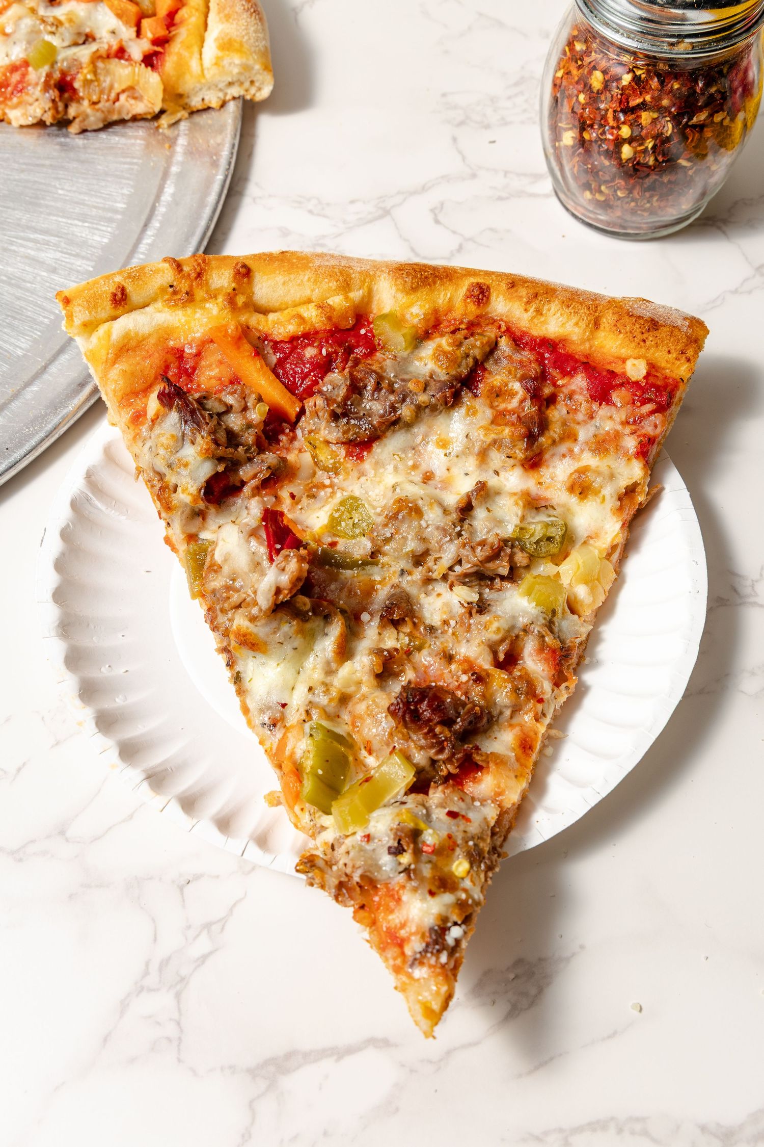 Pizza slice with ground meat and peppers served on a white paper plate.