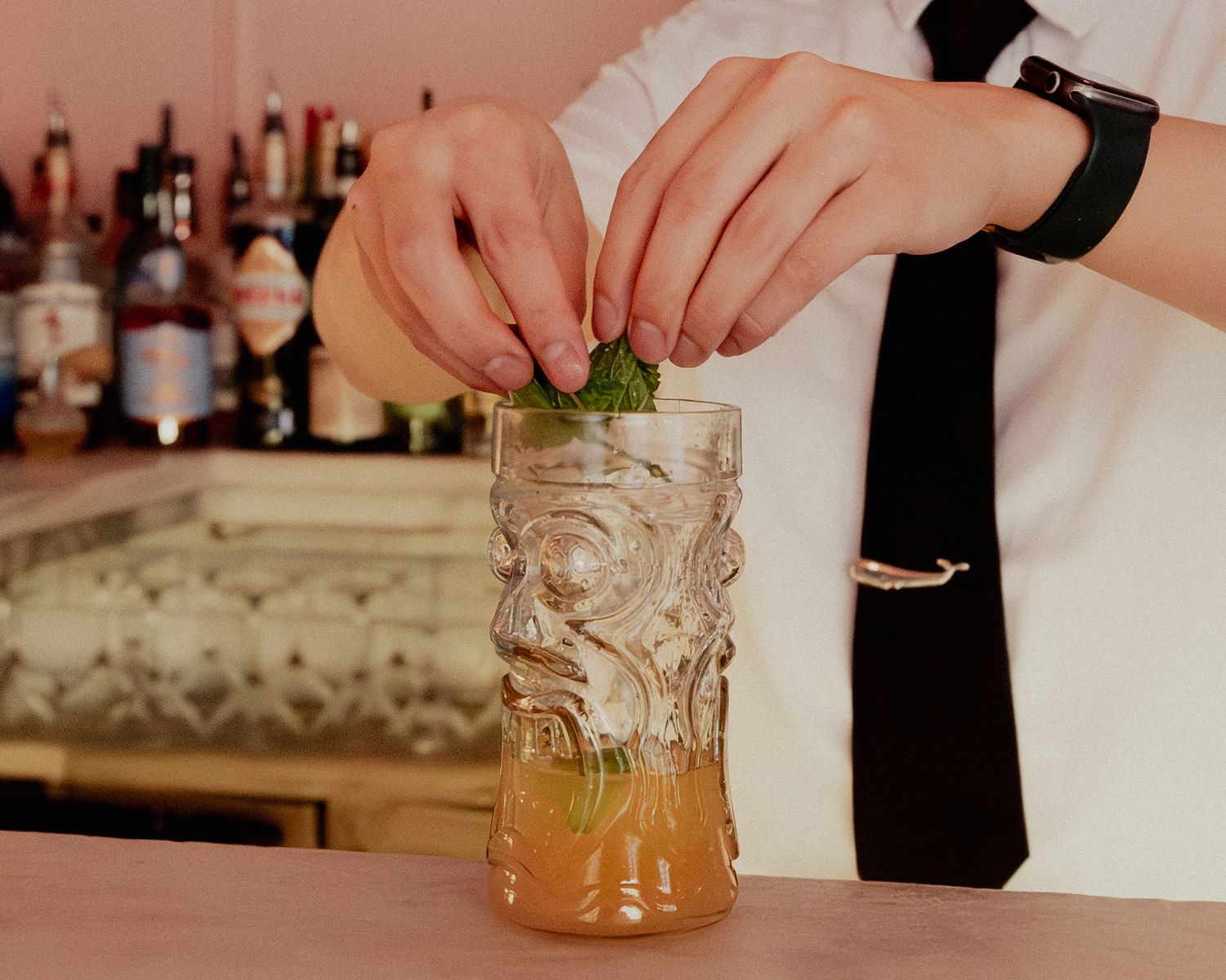 Bartender garnishing a cocktail in a tiki glass with fresh herbs.