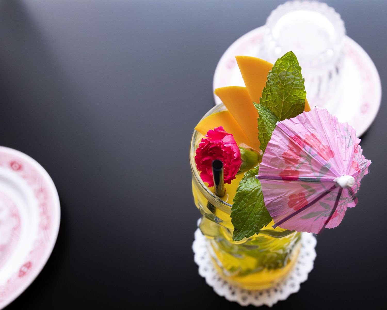 Tropical cocktail garnished with mint, orange, and pink paper umbrella.