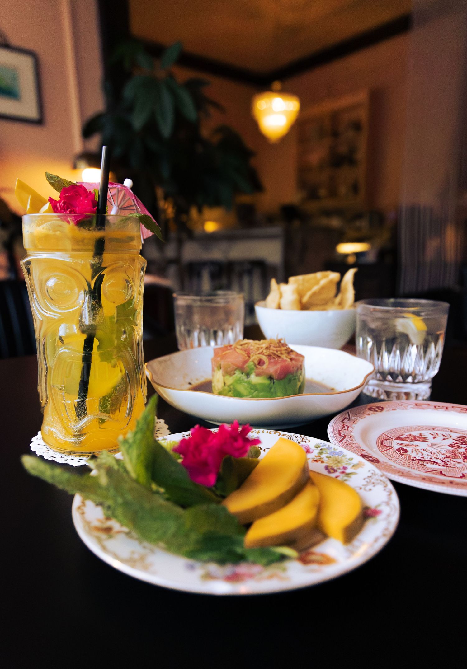 Tropical cocktail and appetizer presentation with colorful garnishes on patterned plates.