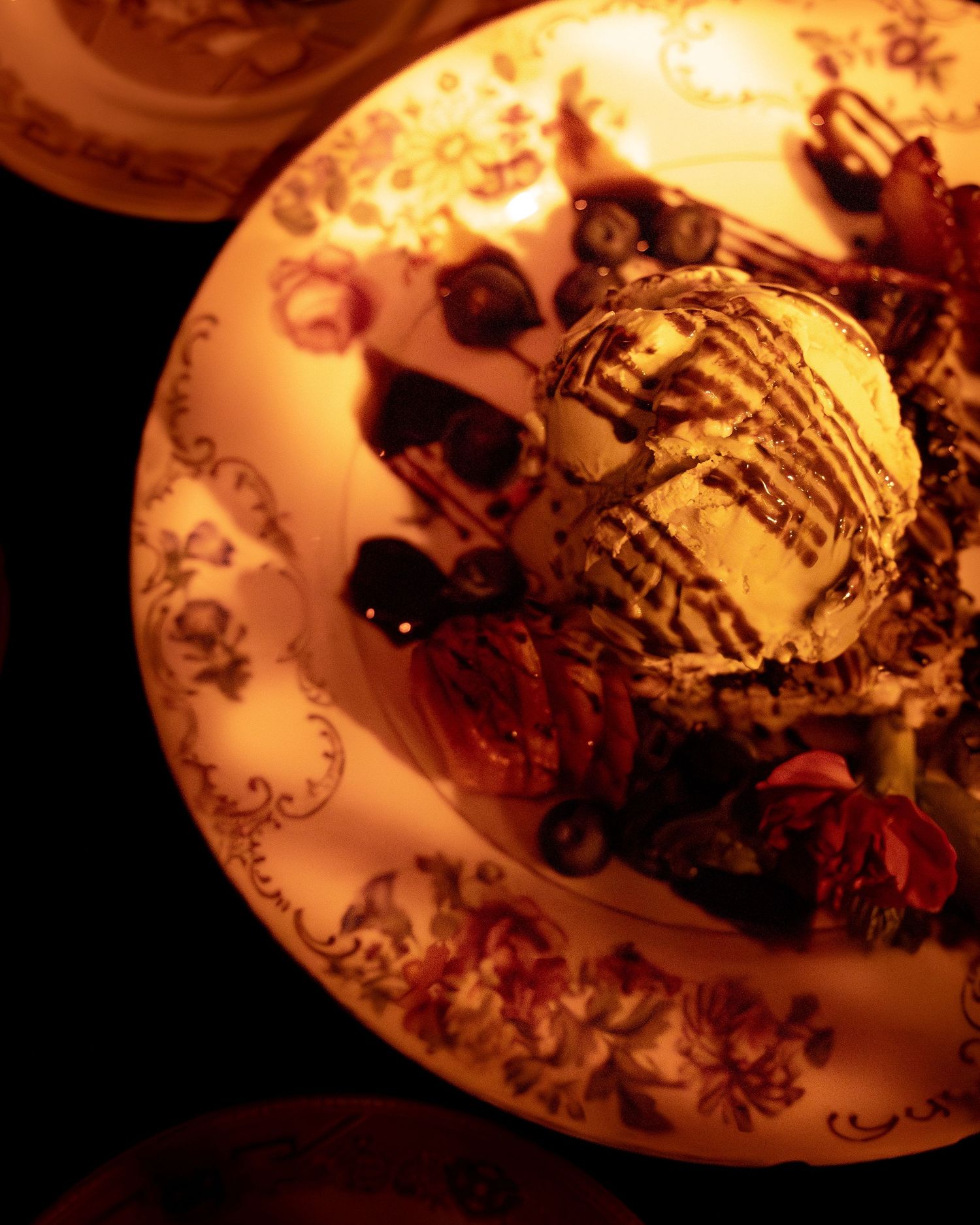 Dessert plate with ice cream and chocolate drizzle in ornate floral china.