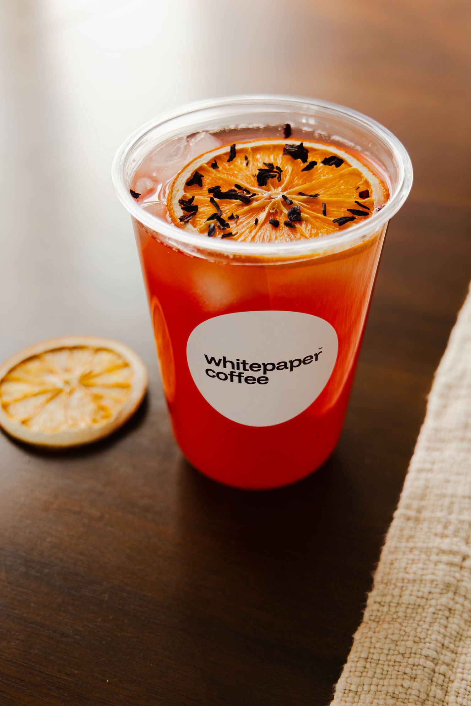A series of four photos showing a citrus-garnished craft cocktail in a clear plastic cup from Whitepaper Coffee.