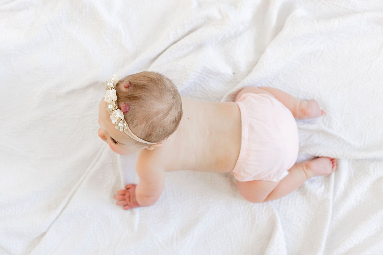 Baby wearing floral headband crawling on white bedding in Springfield, Missouri.