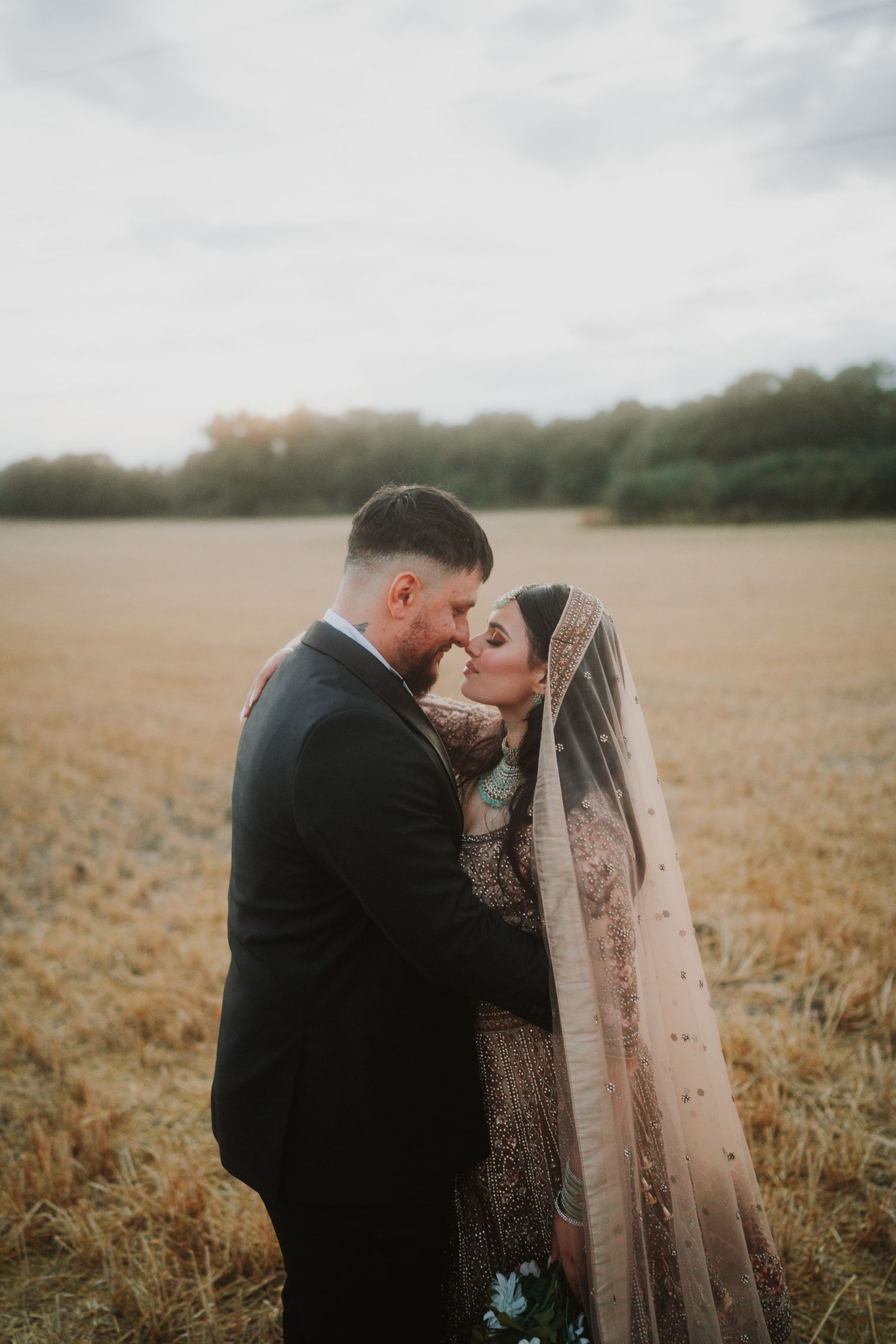 Intimate wedding moment between couple in wheat field during golden hour.
