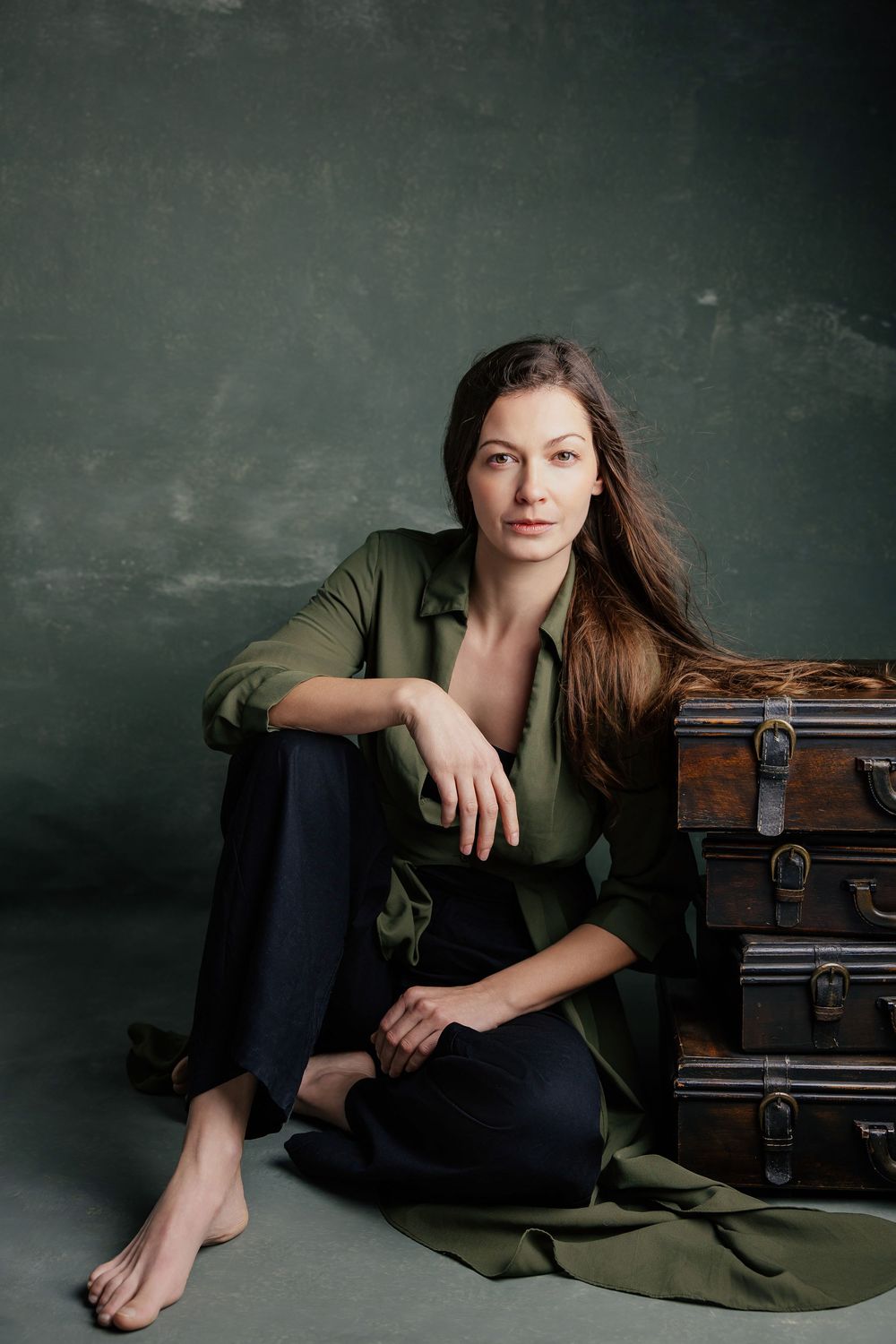 Artistic portrait series against dark textured wall with vintage suitcases and olive green fabric as props.