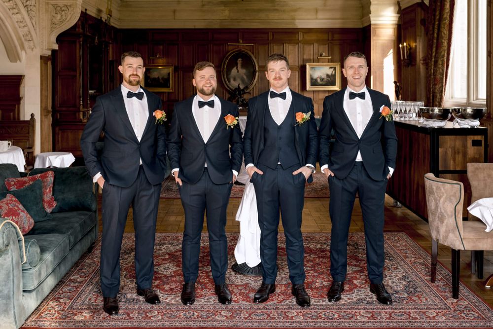 Four groomsmen in black tuxedos pose together in elegant room with vintage furniture. Lough Rynn castle.