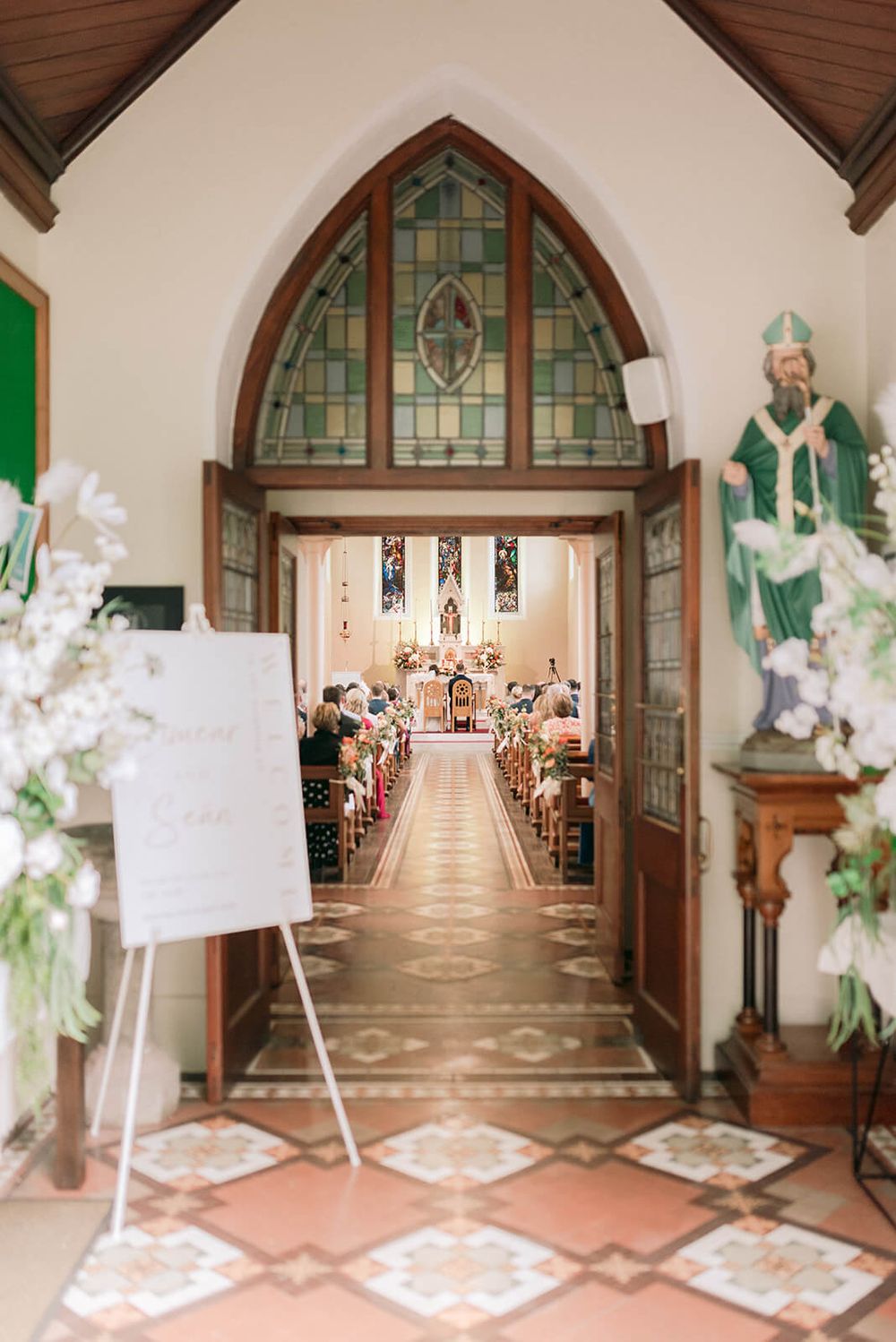 A church entrance with stained glass windows and decorative arches leads to a ceremony filled with guests in county Cavan.